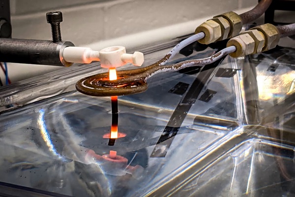 V tomto laboratórnom testovacom zariadení sa tyč zo zliatiny niklu vyťahuje z vodného kúpeľa cez indukčnú cievku.