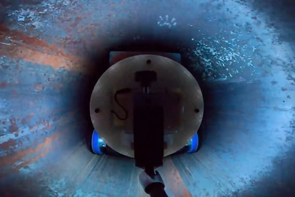 Pohľad zozadu na robota, keď nanáša modrú vazelínu (v tomto teste zastupuje rýchlo tvrdnúcu živicu) do vnútra časti potrubia.