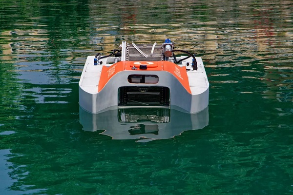 Robotické plavidlo naberá plávajúci odpad, vrátane plastového odpadu na dopravný pás, ktorý ho ukladá do zbernej nádoby vzadu.