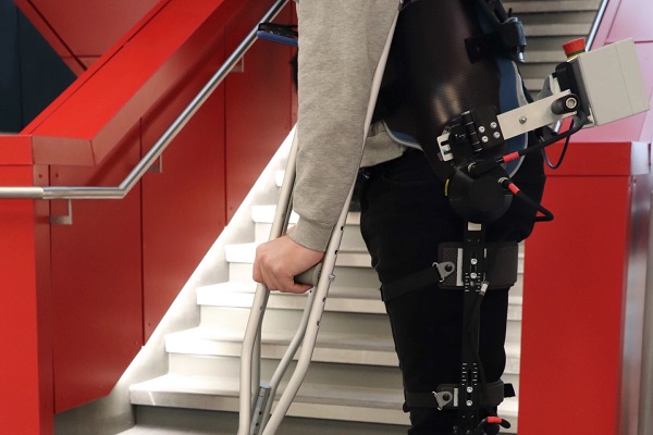 Subjekt s exoskeletónom, ktorý nosí kameru, sa priblíži ku schodisku.